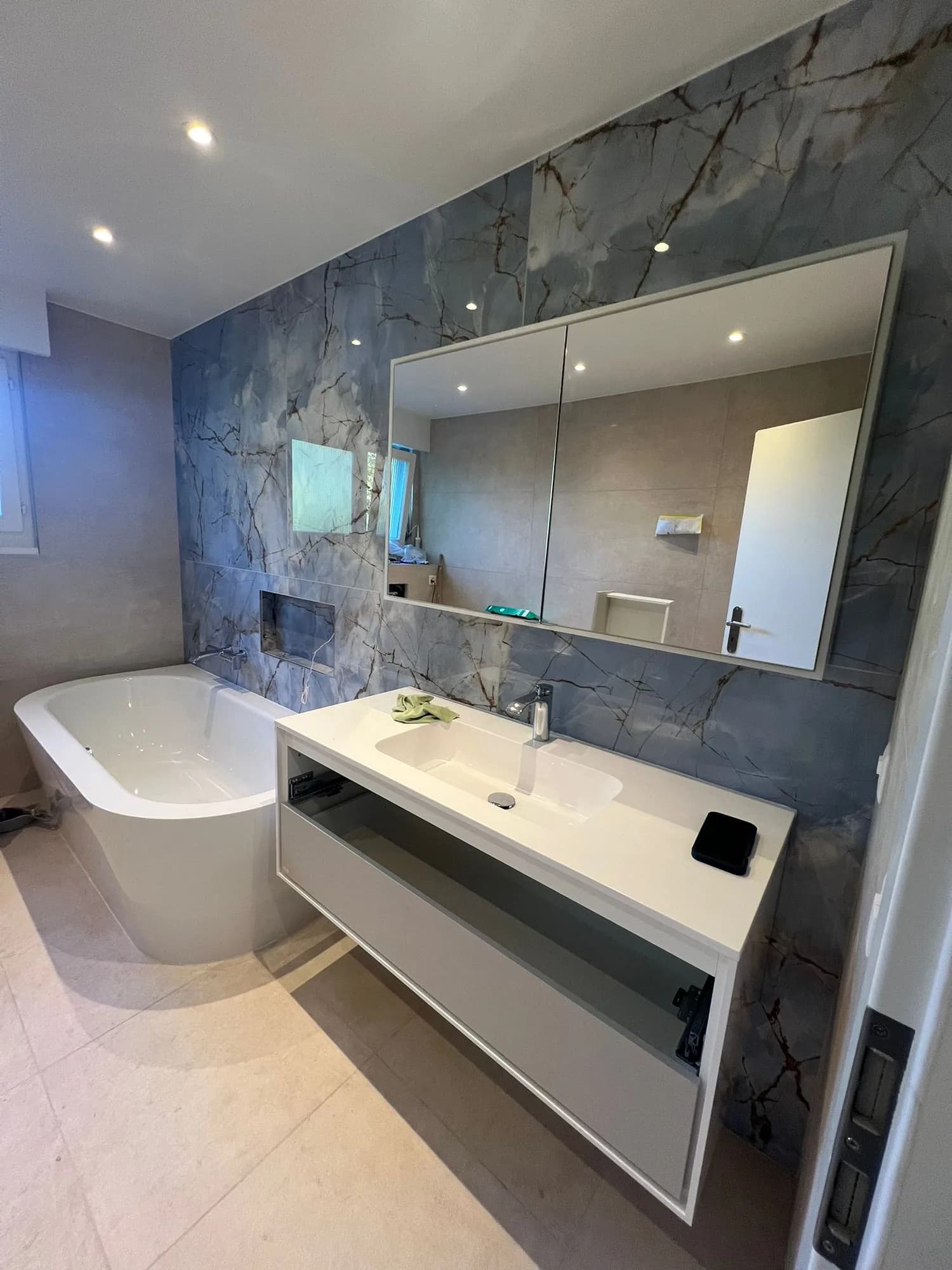 Salle de bain rénovée : baignoire îlot, meuble vasque blanc, grand miroir et carrelage effet pierre