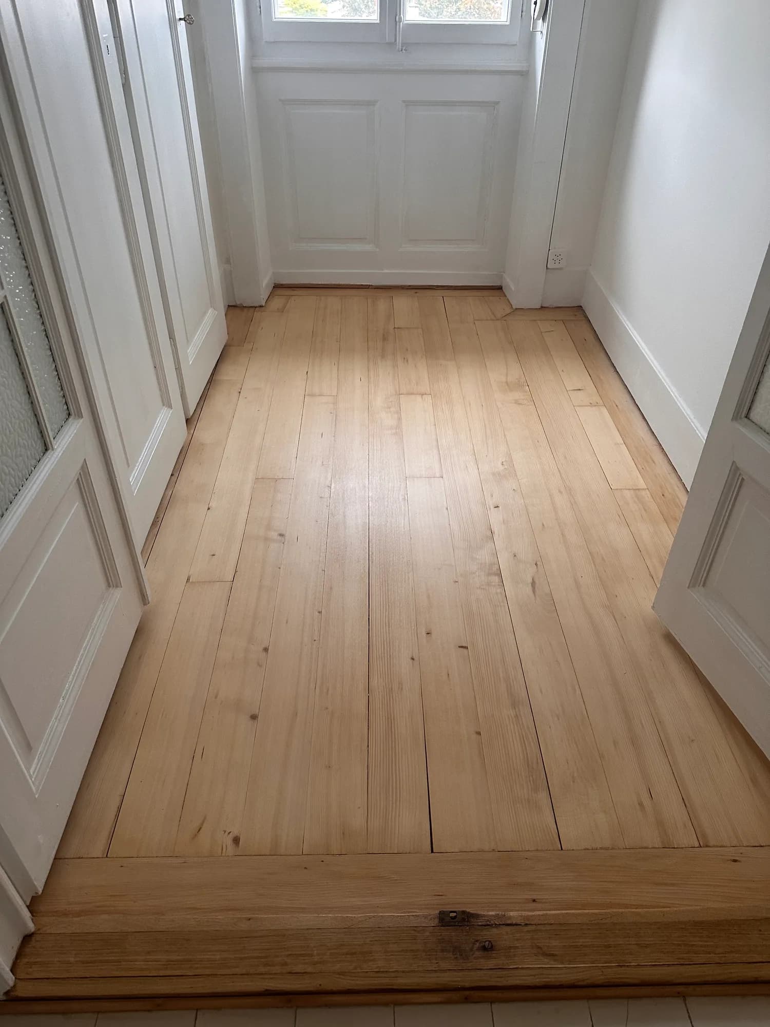 Couloir aux portes blanches, parquet en lames de bois clair poncé
