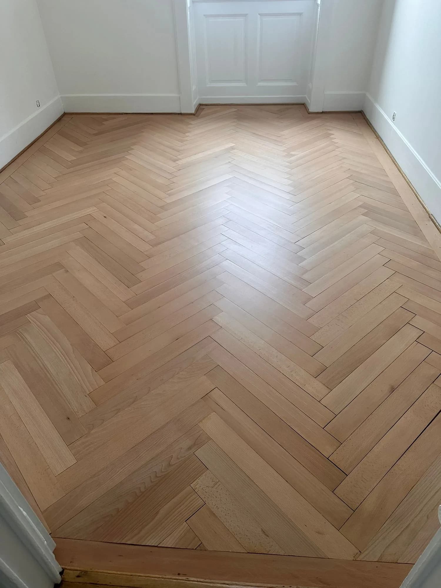 Pièce vide au parquet en chevrons fraîchement vitrifié, murs blancs