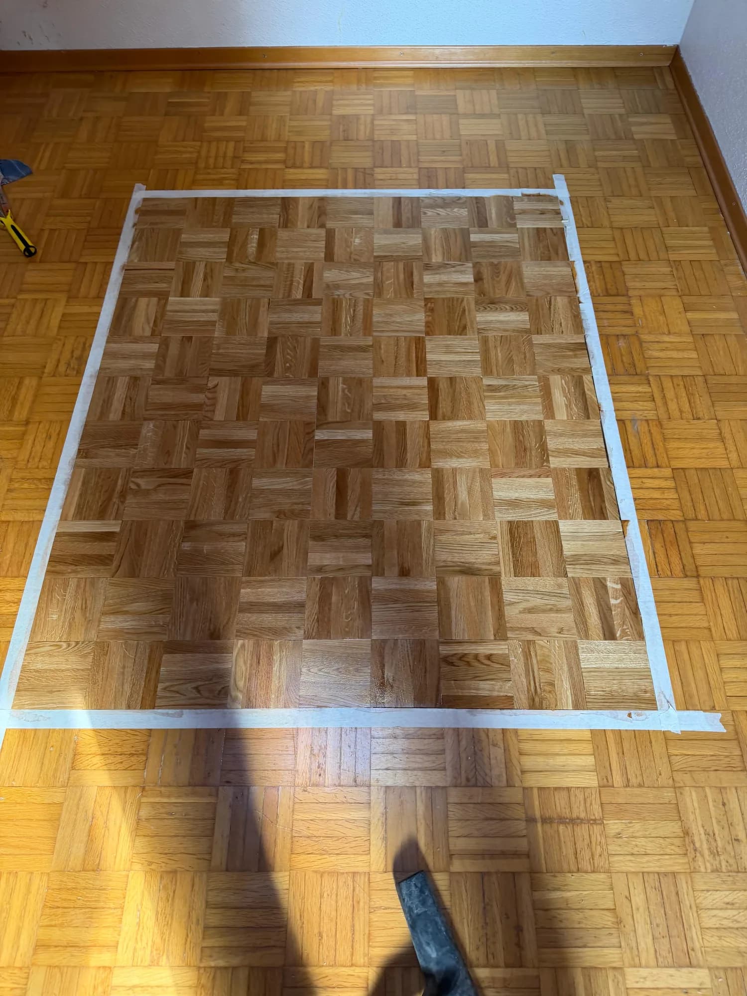 Parquet mosaïque en bois clair, une zone délimitée au ruban adhésif blanc