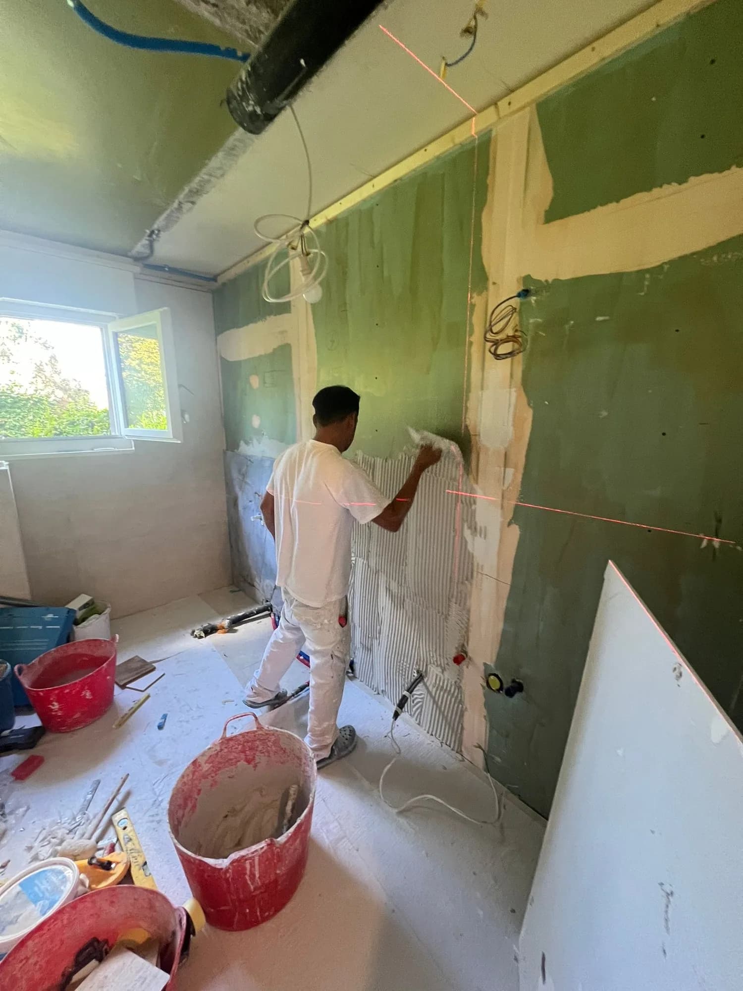 Un ouvrier enduit les joints de plaques de plâtre vertes dans une pièce en travaux