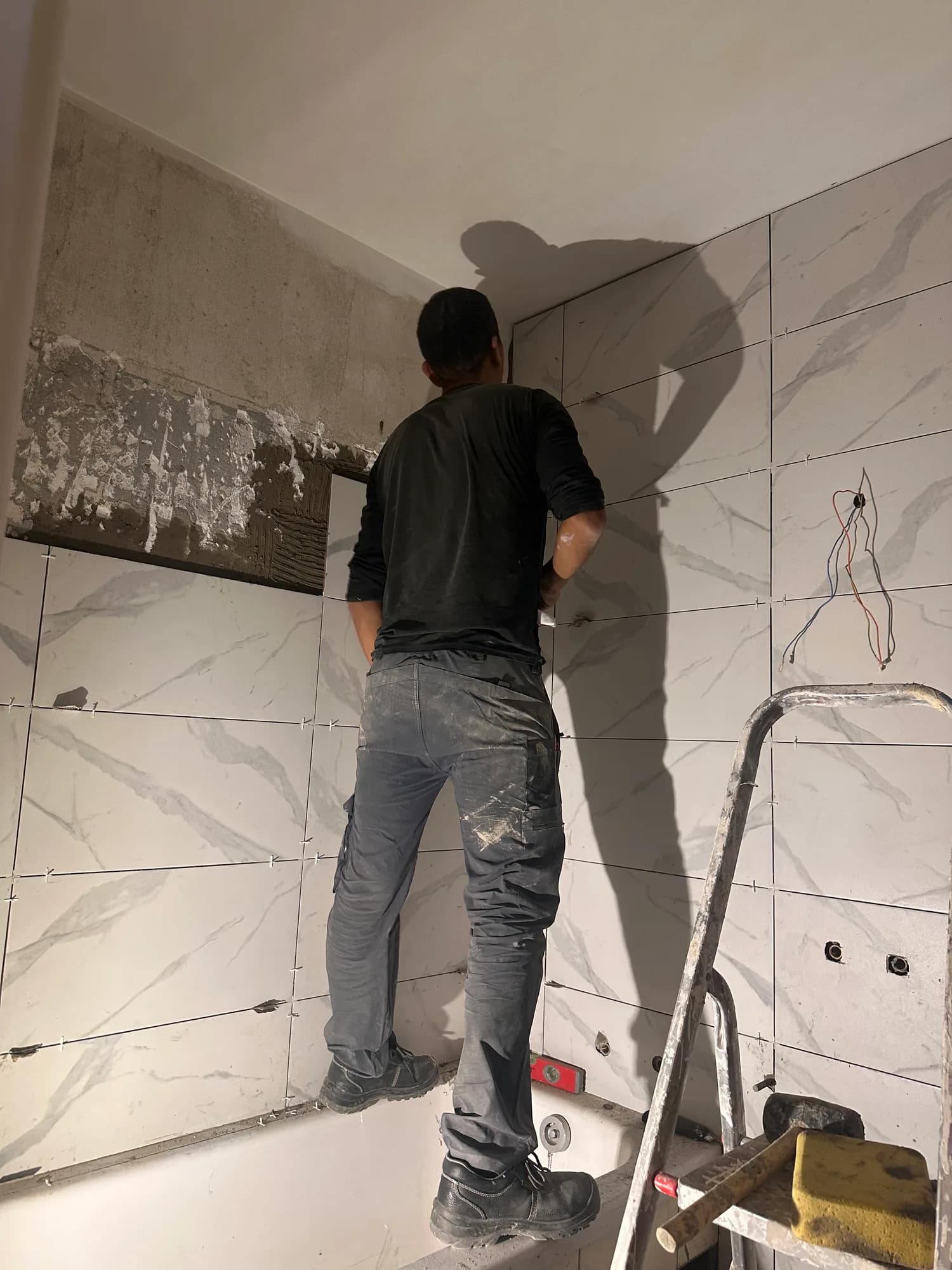 Un ouvrier pose de grands carreaux effet marbre au mur d'une salle de bain