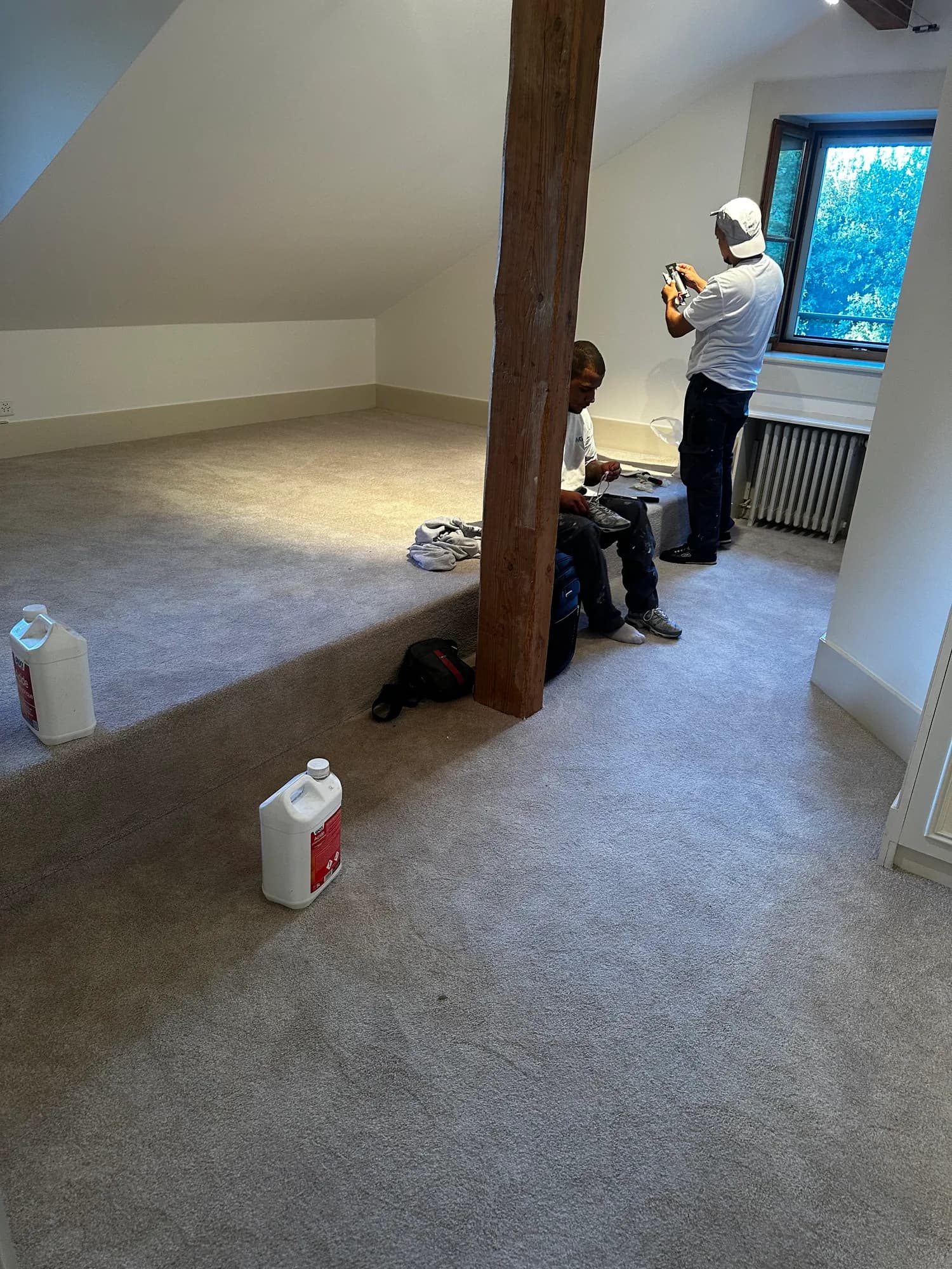 Combles recouverts d'une moquette grise neuve, deux ouvriers près d'une poutre